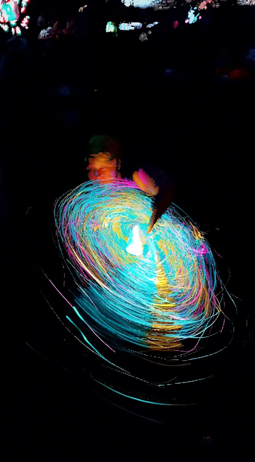 A performer surrounded by vivid cyan, pink, and gold light trails in a photograph captured with FlowTrace
